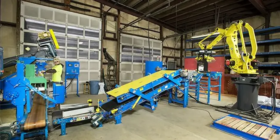 Worker in a hi-vis vest operates a blue bagging line with a yellow robot and conveyors.