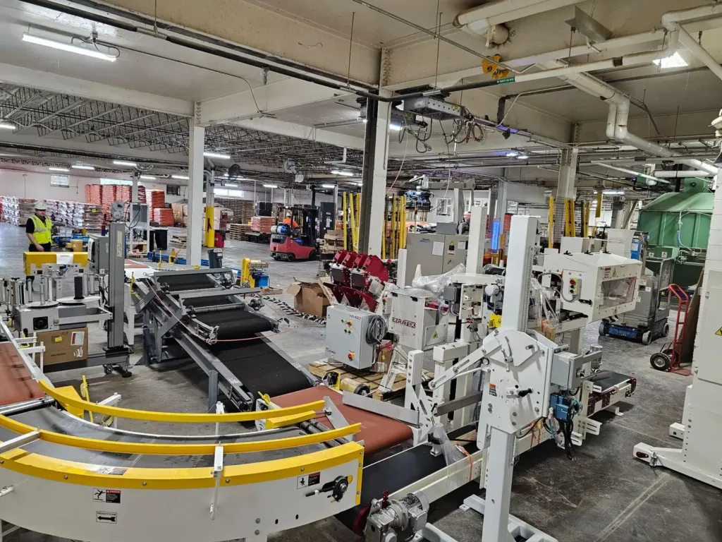 Factory floor during install with conveyors, bagging machinery, stacked materials, and a forklift.