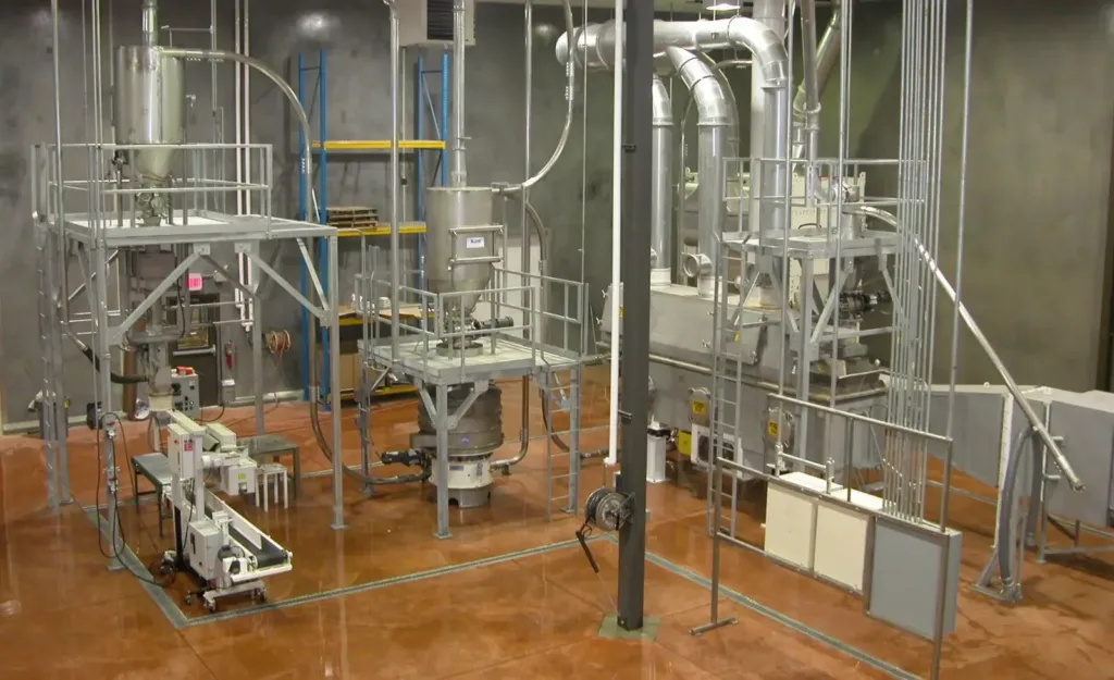 Pneumatic conveying system with elevated hoppers, a rotary sifter, and platforms on a polished brown floor.