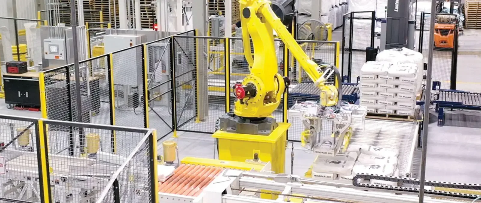 Yellow robotic arm palletizes white Minspar 200 bags inside a safety-fenced packaging cell.