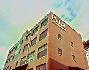 Multi-story brick building exterior with large white Parisi Artisan Coffee signage under a cloudy sky.