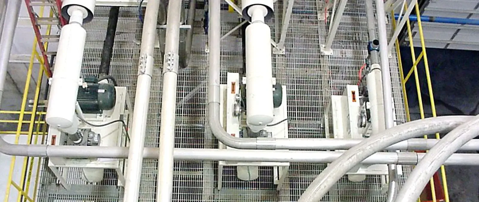 Overhead view of three green-motor blower packages with large silver piping on a grated mezzanine.